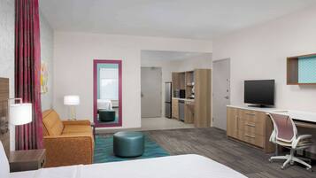 Habitación de hotel con cama, escritorio, televisor, kitchenette y baño.