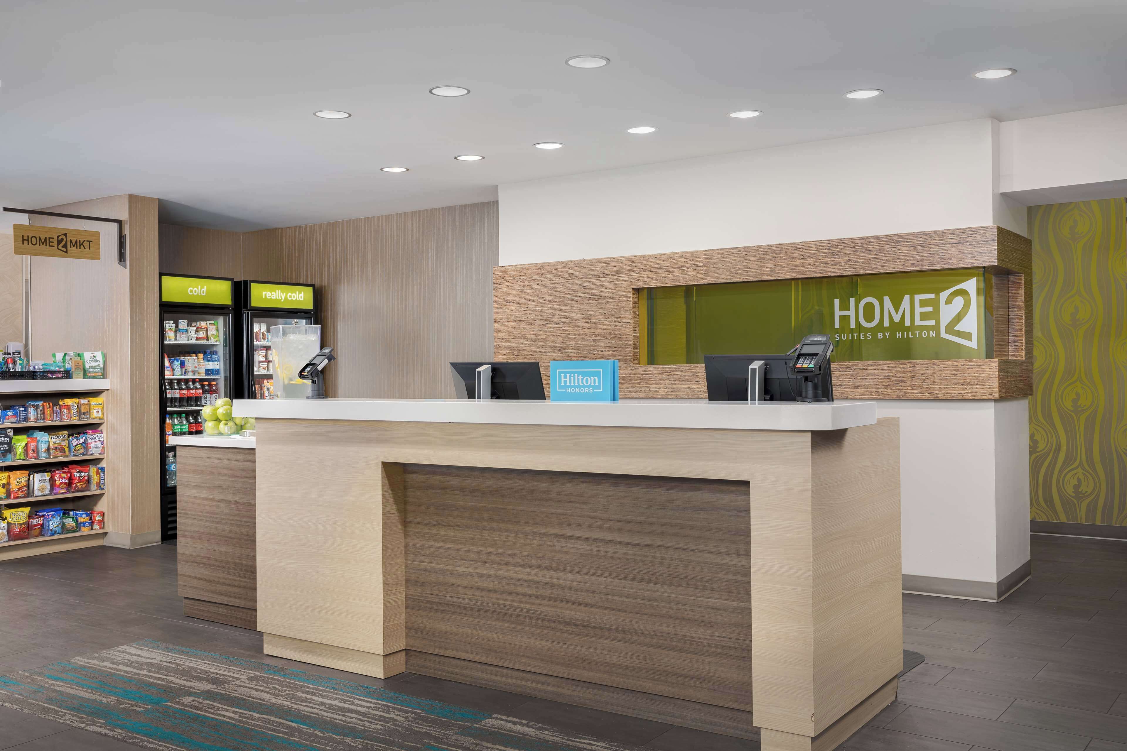 A hotel reception desk with a modern design, a minibar, and a self-service beverage station.