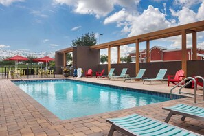 A swimming pool with lounge chairs and umbrellas, surrounded by a brick patio and wooden pergola. - Home2 Suites by Hilton Clermont (Clermont)