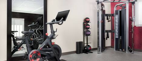 Une salle de sport équipée de vélos d’exercice, d’une machine de musculation et d’un miroir.