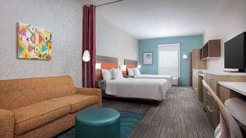 Quarto de hotel com duas camas, um sofá, uma televisão e um quadro na parede.