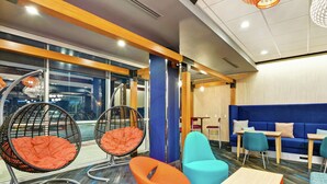 A modern office space with a blue sofa, orange and blue chairs, and a wooden table. - Tru by Hilton Richmond (Richmond)