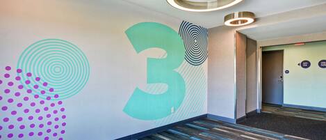 Un pasillo con un gran número 3 en la pared, una alfombra estampada y una puerta con el símbolo de número.