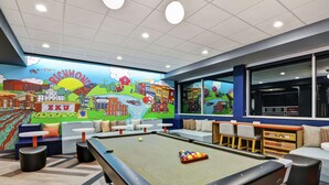 A pool table with a colorful mural in the background, seating areas, and a view through large windows. - Tru by Hilton Richmond (Richmond)