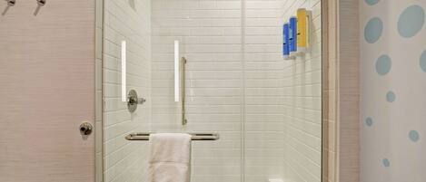 Un baño moderno con ducha de vidrio, paredes de azulejos blancos, un perchero y artículos de aseo en un estante.