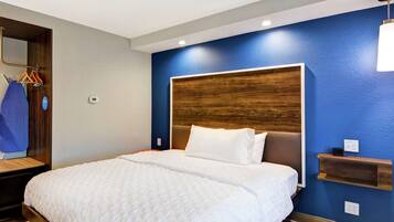 Una habitación de hotel moderna con una cama grande, un cabecero de madera, una pared de acento azul y un pequeño estante de madera.