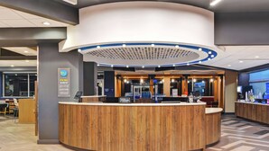 A modern hotel reception area with a wooden reception desk, a circular light fixture above, and a view of the lobby. - Tru by Hilton Richmond (Richmond)