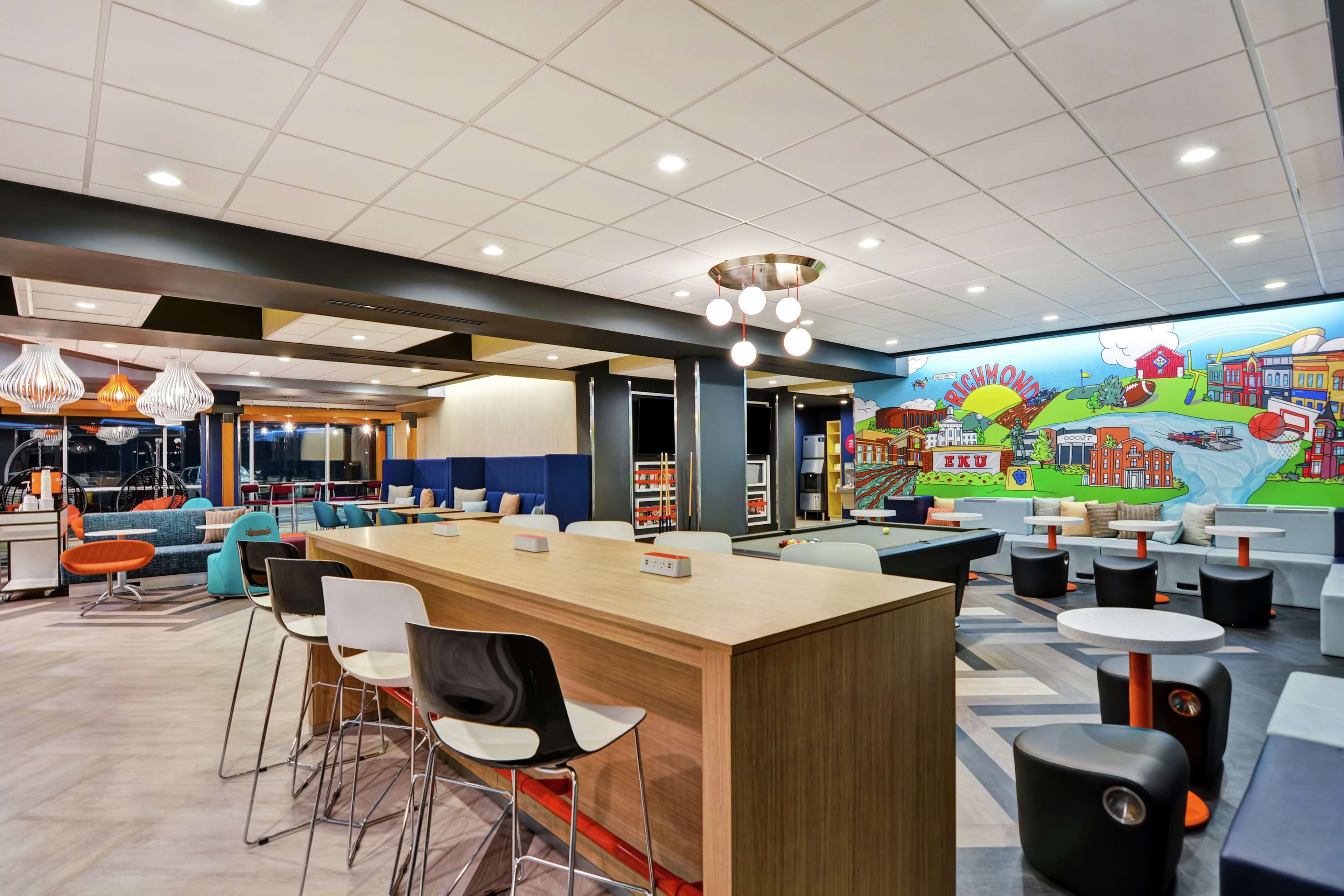 A modern bar area with a long counter, multiple seating options, and a mural depicting a cityscape.