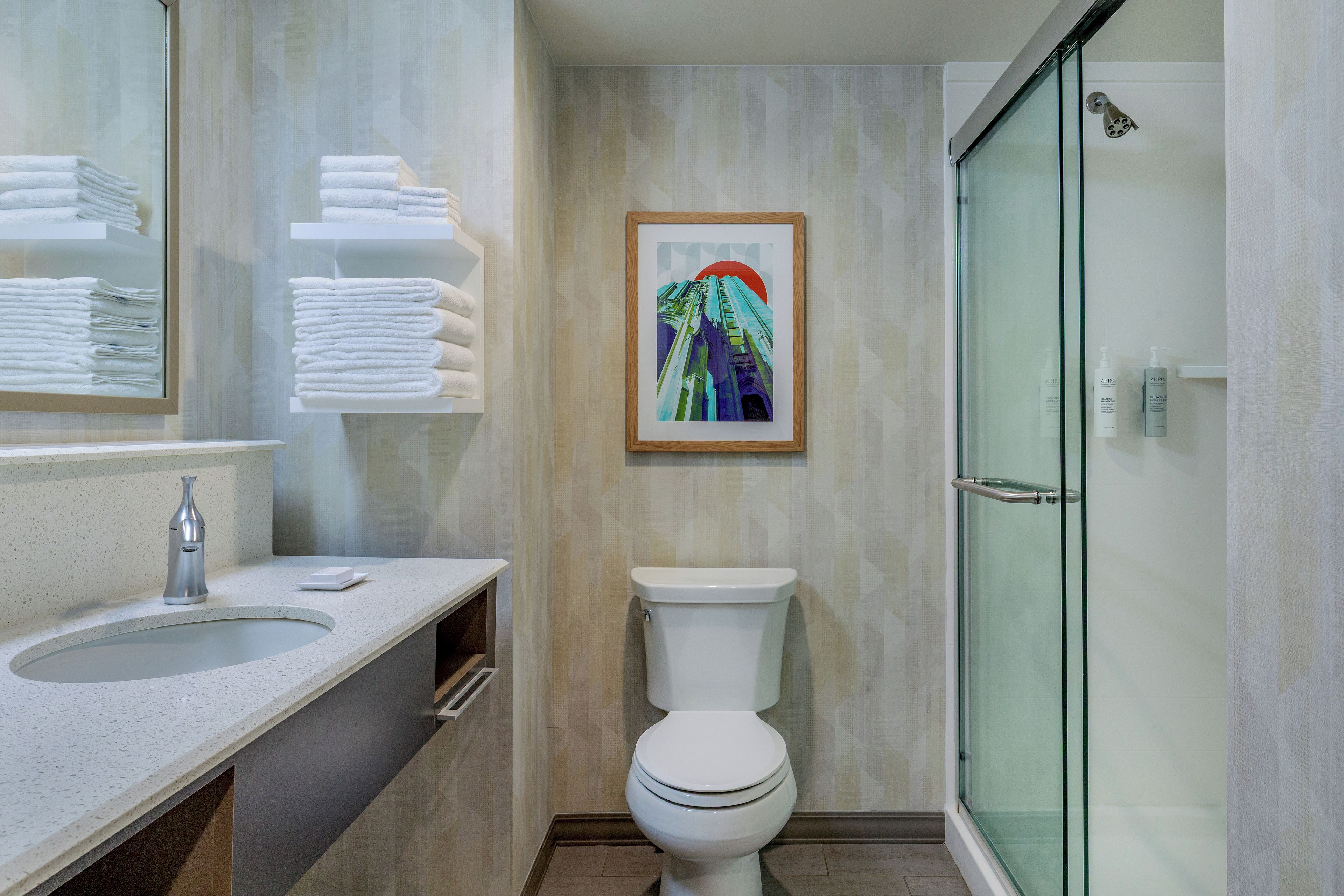 A modern bathroom with a glass shower enclosure, a toilet, and a sink with a towel rack.