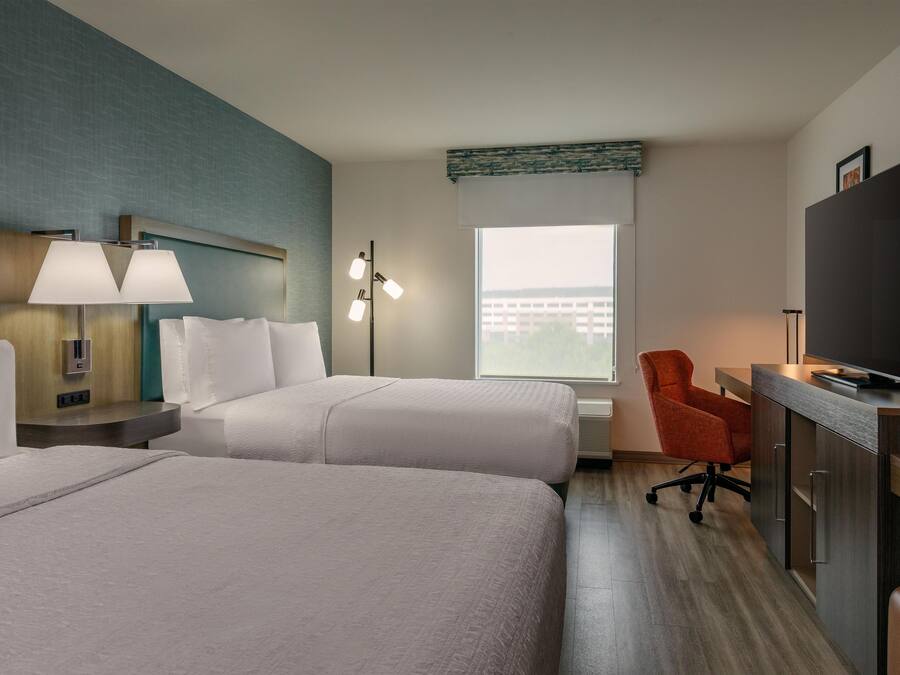 Une chambre d’hôtel avec deux lits, un bureau avec une télévision, une chaise et une fenêtre donnant sur des immeubles.