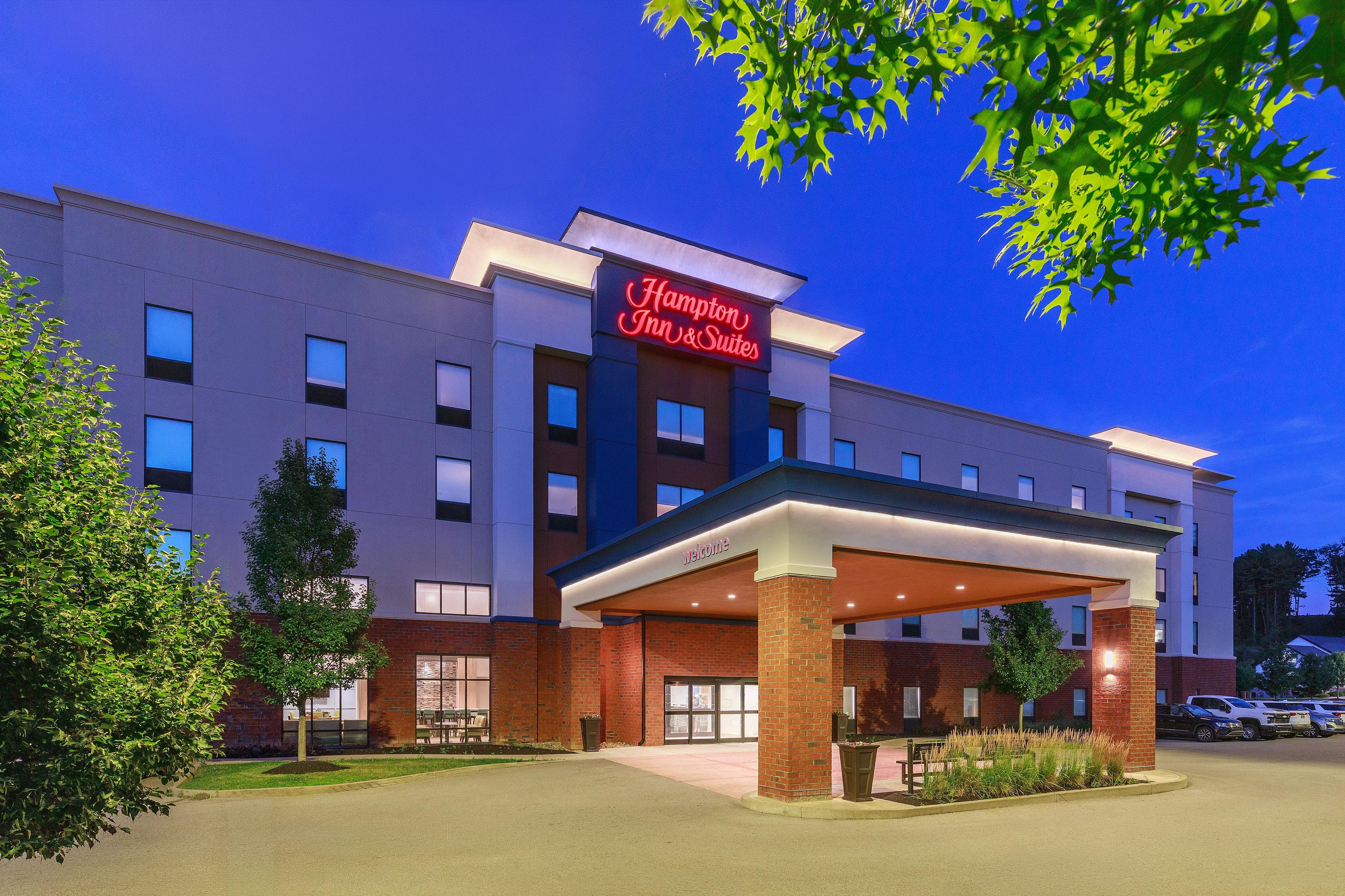 A Hampton Inn & Suites hotel with a covered entrance, multiple windows, and a parking area.