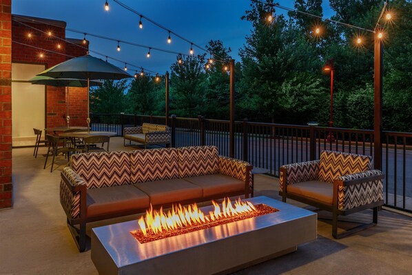 An outdoor patio with a fire feature, seating, and string lights.