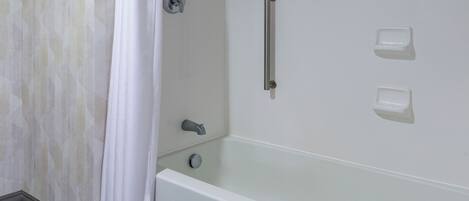 A bathroom with a bathtub, a shower curtain, a grab bar, and two soap dispensers.
