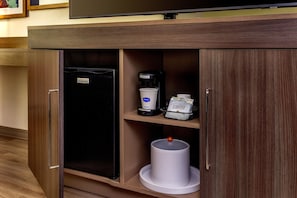 A hotel minibar with a coffee machine, a coffee pod dispenser, and a trash can.