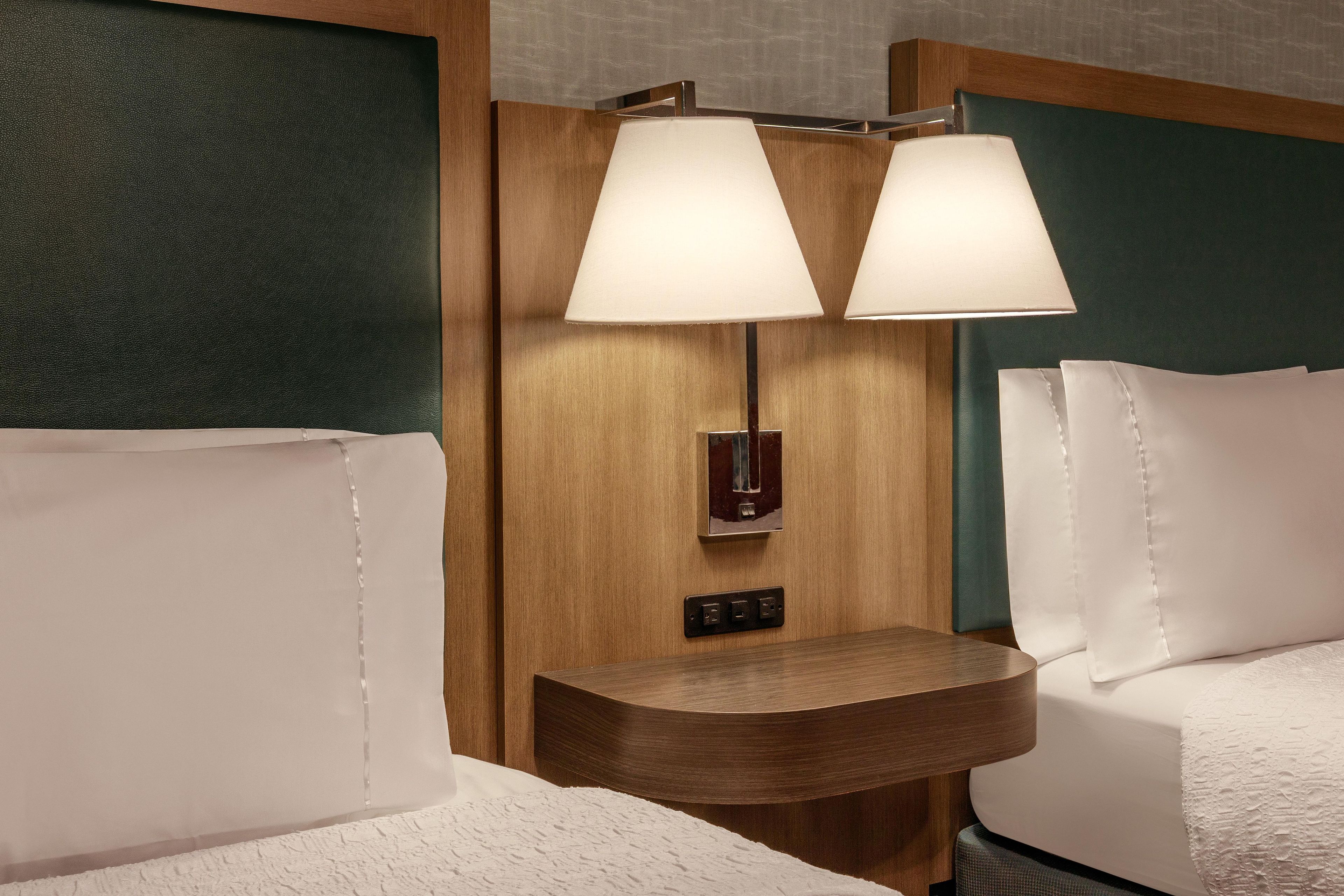 A hotel room with a wooden headboard, two bedside lamps, a nightstand, and a bed with white linens.