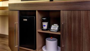 A hotel minibar with a coffee machine, a coffee pod dispenser, and a trash can.