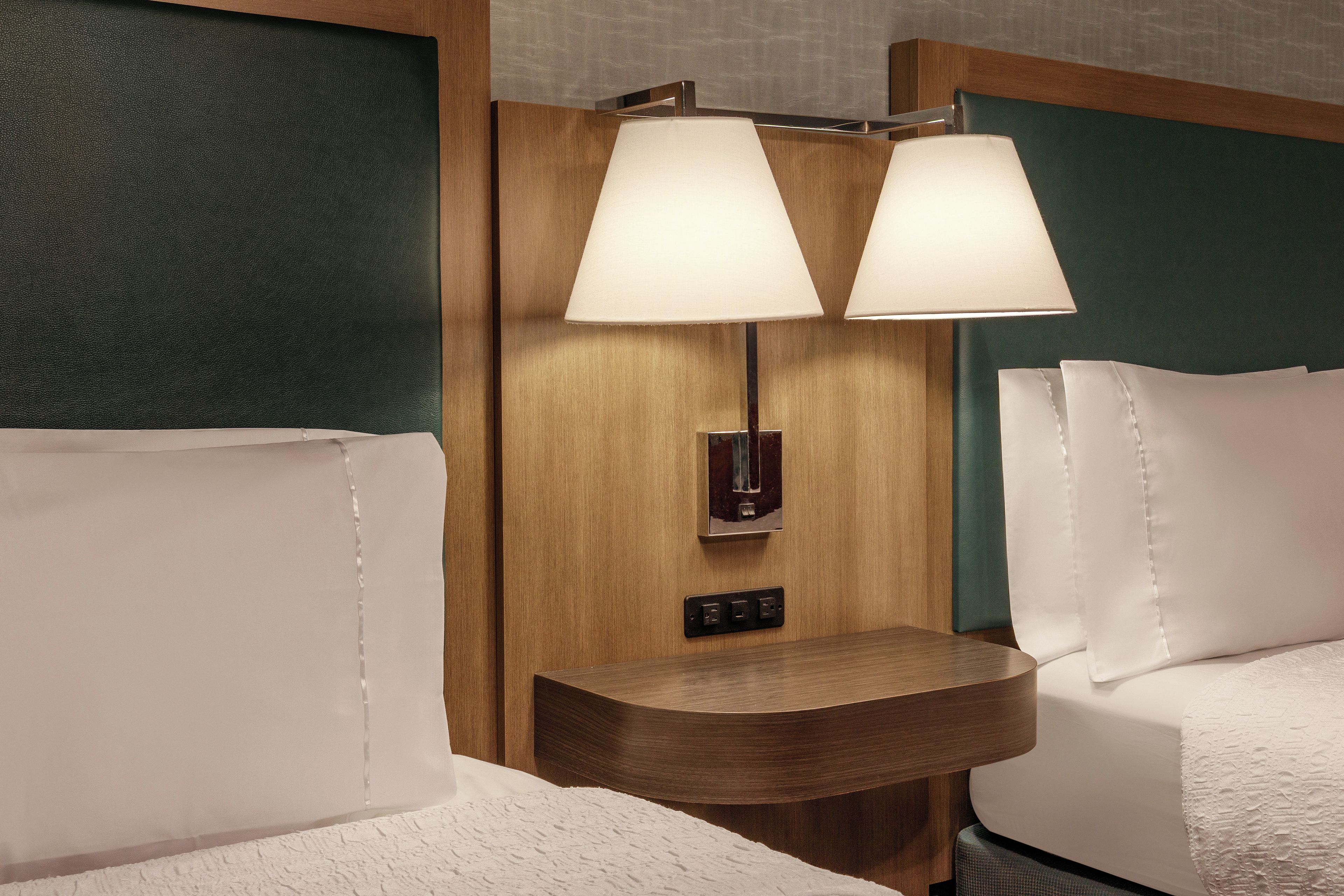 A hotel room with a wooden headboard, two bedside lamps, a nightstand, and a bed with white linens.