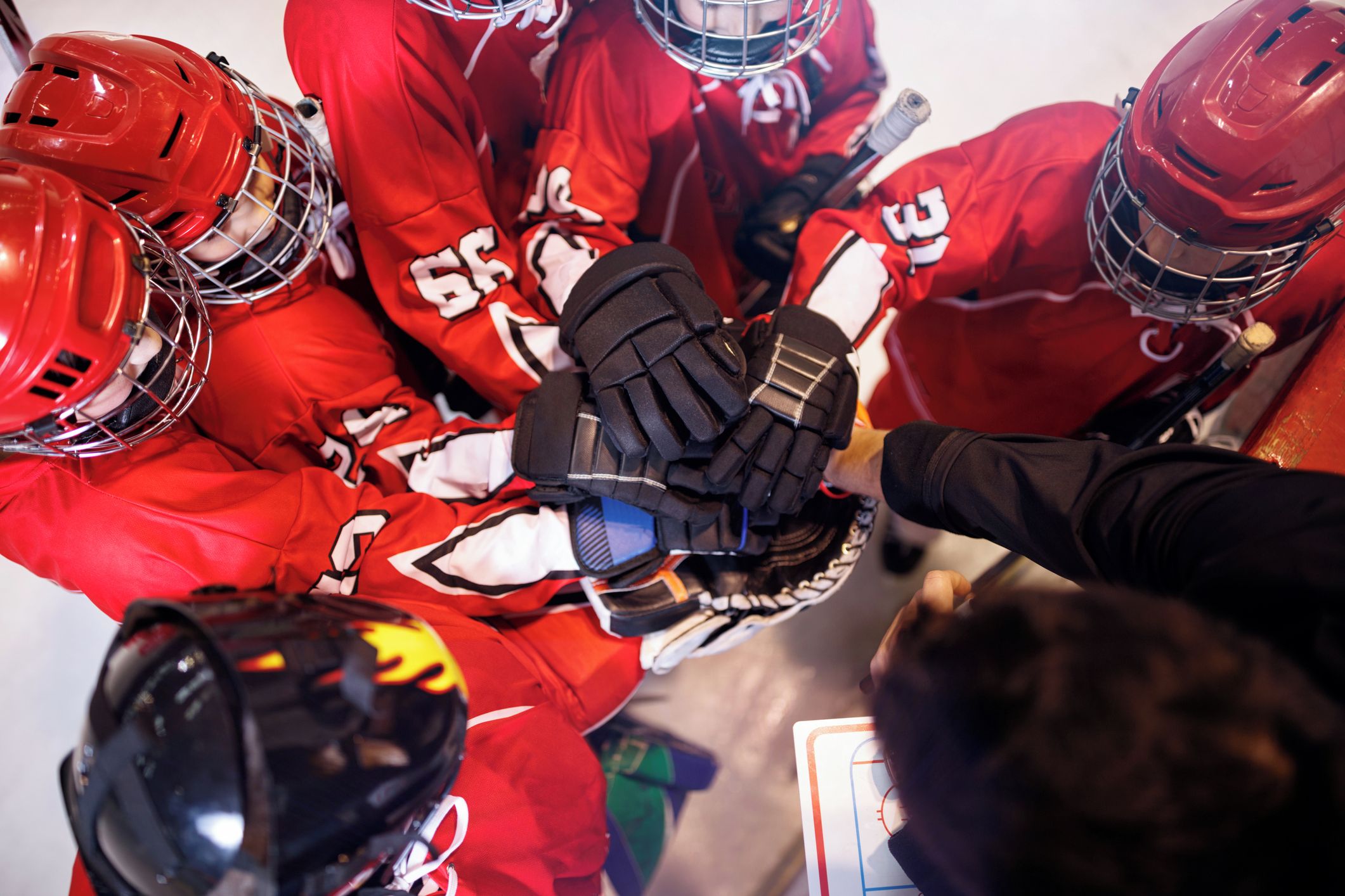 A group of hockey players in red uniforms with helmets and gloves, huddling together.