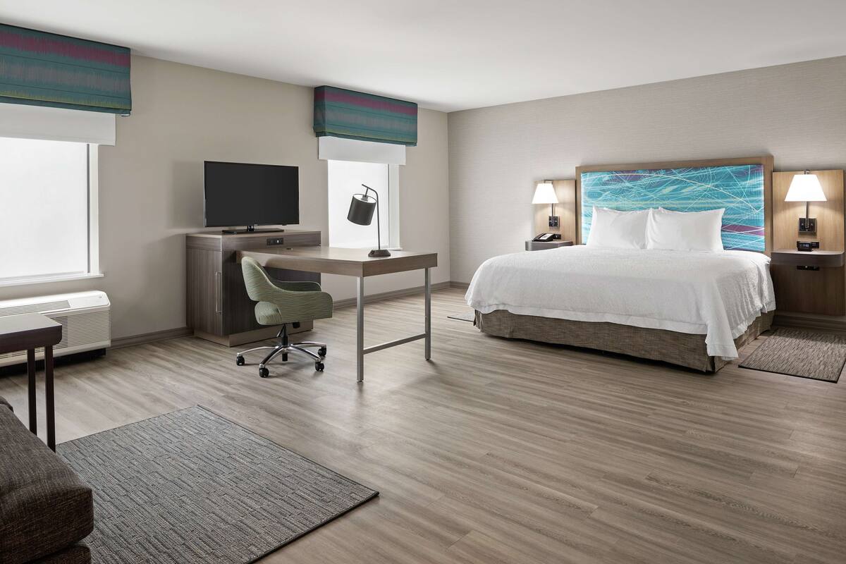 A hotel room with a bed, desk, chair, TV, and two bedside lamps.