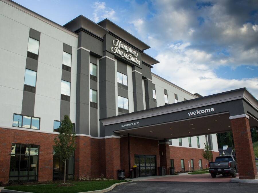 A Hampton Inn & Suites building with a clear entrance, a welcome sign, and a parking area with a truck.