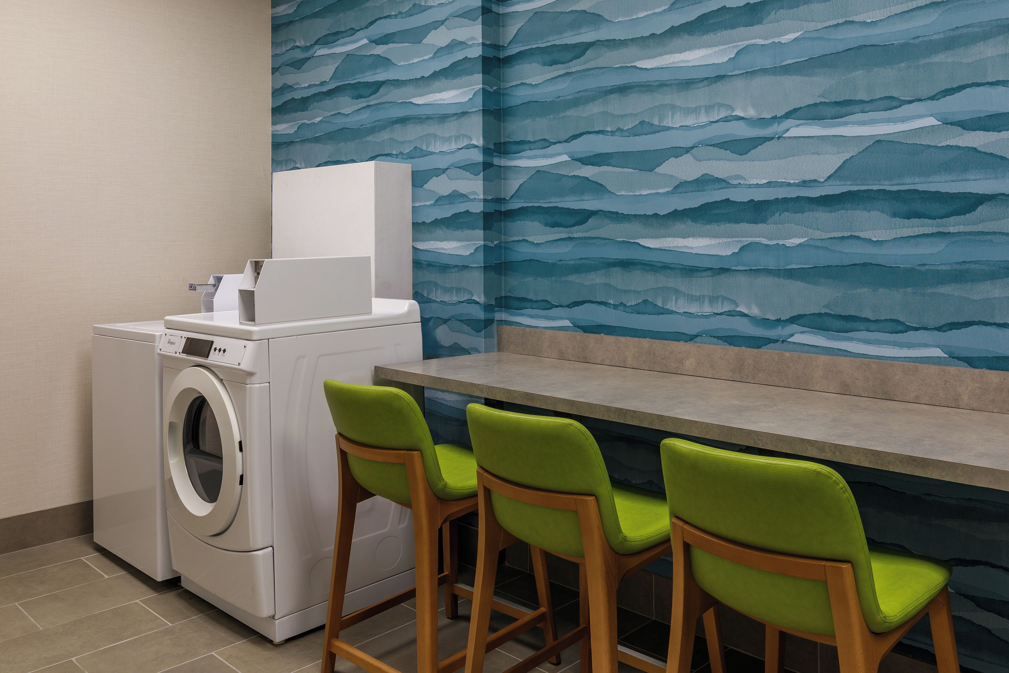 A laundry area with a washing machine, a table, and three green chairs.