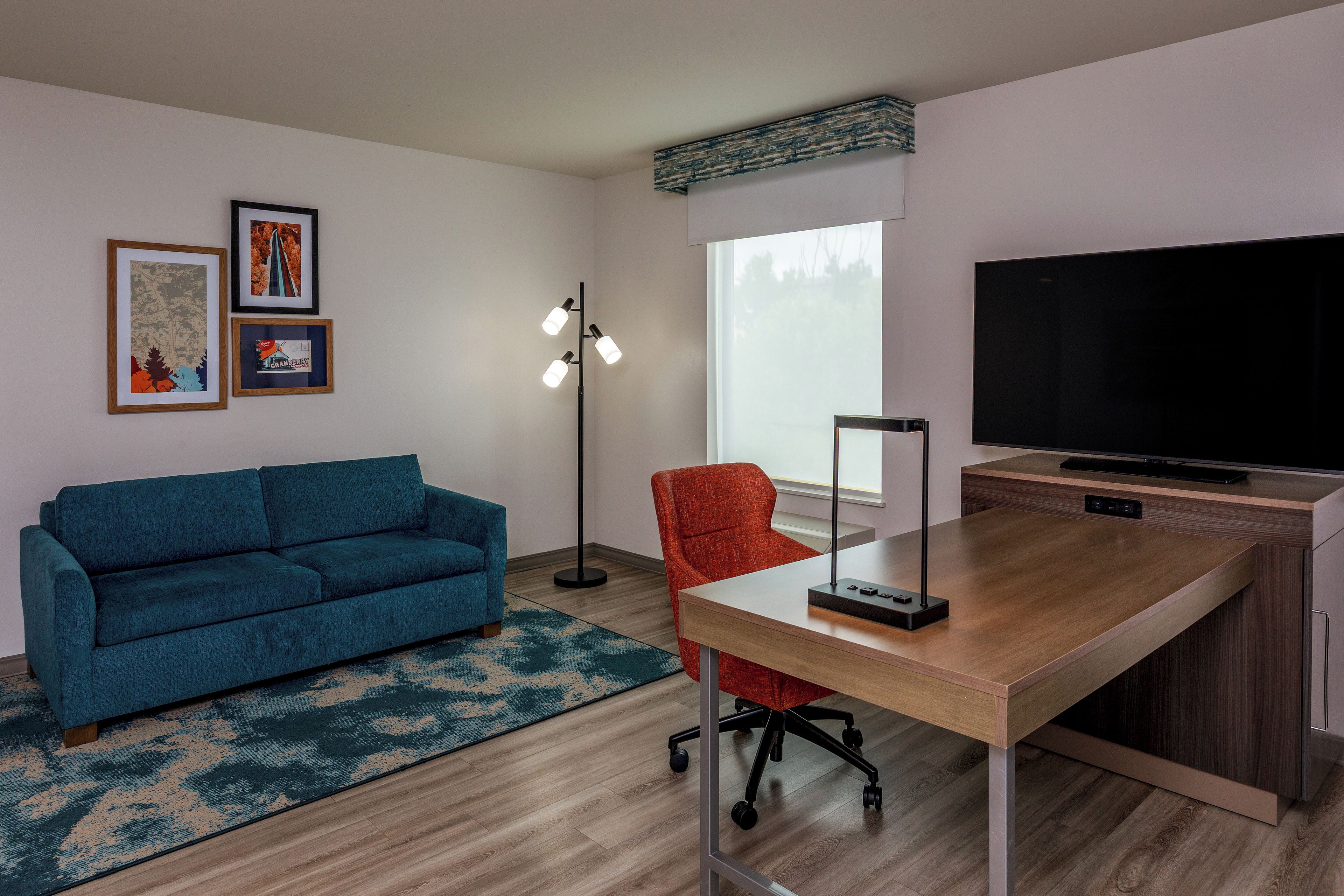 Una sala de estar moderna con un sofá azul, un sillón rojo, un escritorio de madera, un televisor de pantalla plana y una lámpara de pie.