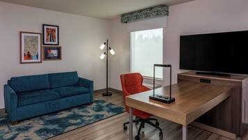 Una sala de estar moderna con un sofá azul, un sillón rojo, un escritorio de madera, un televisor de pantalla plana y una lámpara de pie.