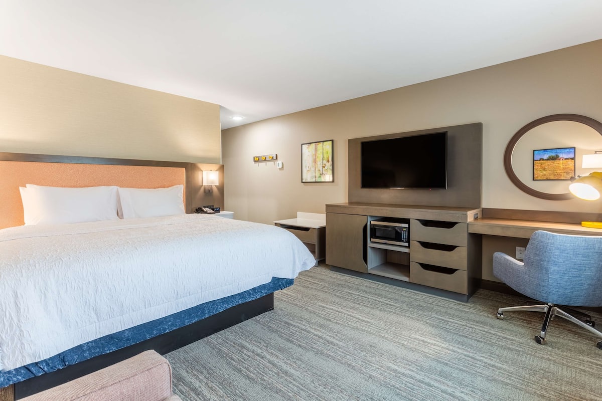 Quarto de hotel com uma cama grande, uma escrivaninha com televisão de tela plana, uma cadeira e uma pequena luminária de mesa.