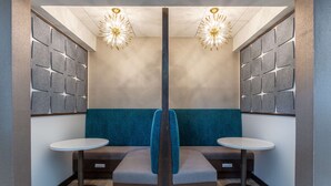 A modern, symmetrical room with a central seating area, two small round tables, and decorative wall panels. - Hampton Inn & Suites Guymon (Guymon)