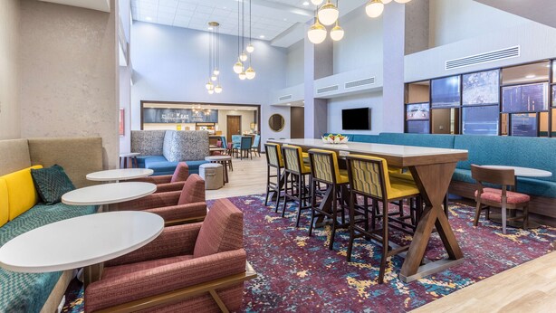 A modern hotel lobby with a central seating area, a bar, and a large screen. - Hampton Inn & Suites Guymon (Guymon)
