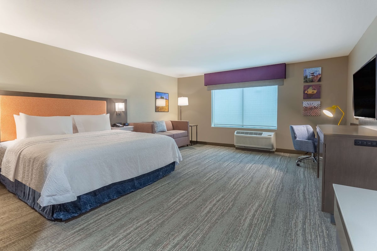 Quarto de hotel com uma cama grande, uma escrivaninha, uma cadeira e uma janela.