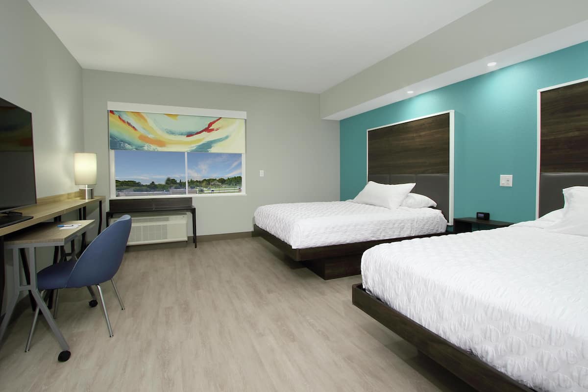 Ett hotellrum med två sängar, ett skrivbord med en stol, en TV och en tavla som föreställer ett landskap.