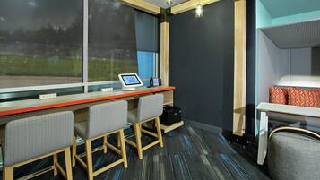 Habitación de hotel con escritorio, dos sillas, una computadora y una cama con almohadas estampadas.