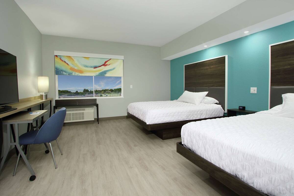 Ett hotellrum med två sängar, ett skrivbord med en stol, en TV och en tavla på väggen.
