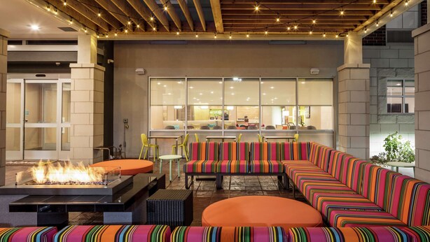 A modern outdoor seating area with a fire feature, wooden ceiling beams, and a view of the interior. - Home2 Suites by Hilton Dayton/Centerville (Dayton)