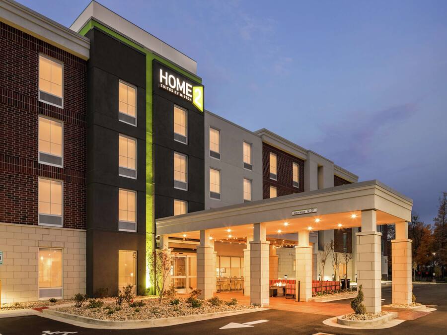 A hotel with a modern facade, a covered entrance, and a sign indicating 'Home Suites by Hilton'.