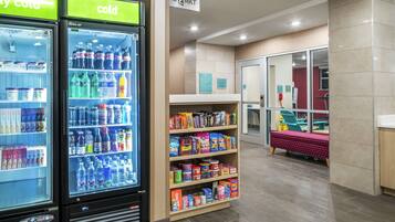A clean, modern hotel lobby with a self-service beverage machine, snack shelves, and a visible reception area.
