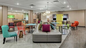 A modern hotel lobby with a reception desk, seating areas, and a children's play zone. - Home2 Suites by Hilton Dayton/Centerville (Dayton)