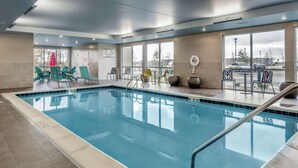A swimming pool with lounge chairs and tables, large windows, and a view of the parking lot. - Home2 Suites by Hilton Dayton/Centerville (Dayton)