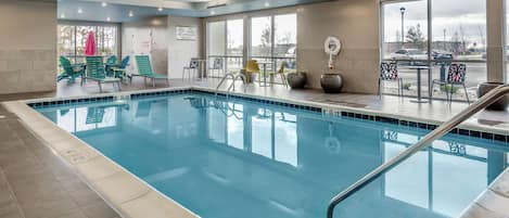 Una piscina con sillas de descanso y mesas, ventanas amplias y vista al estacionamiento.
