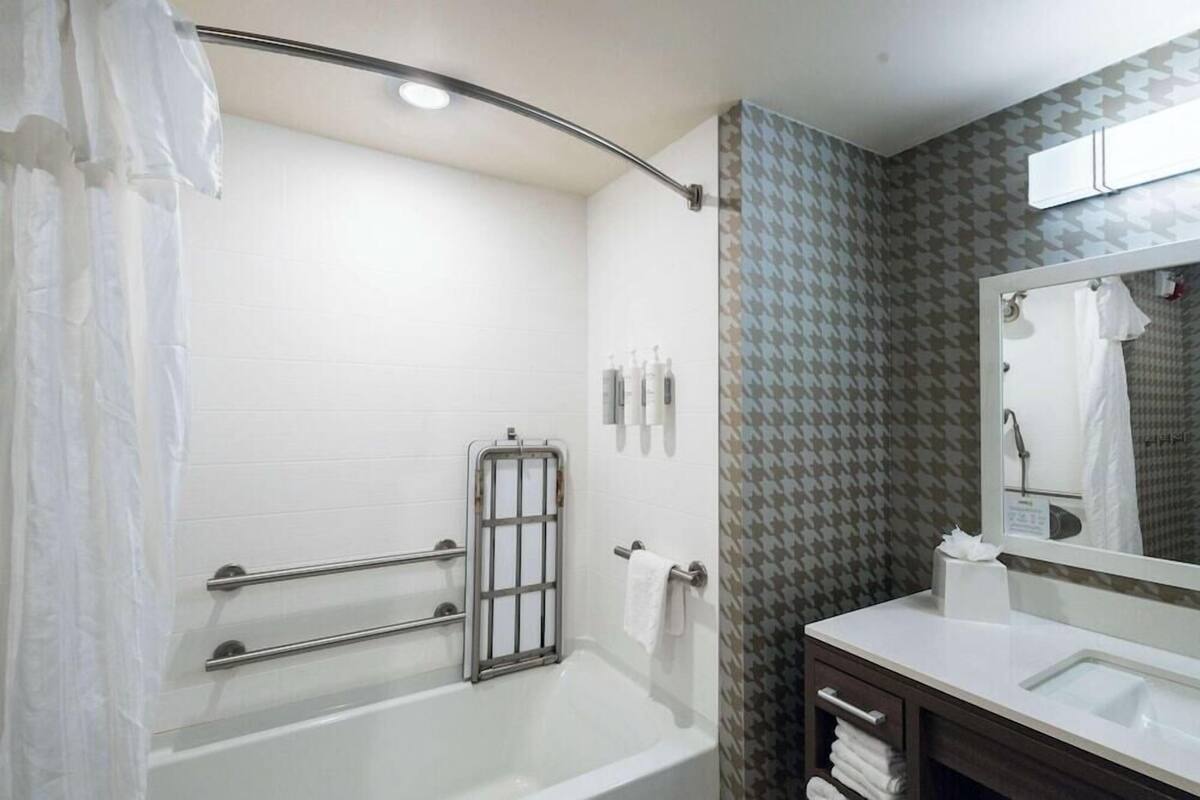 Ein Badezimmer mit einer Badewanne, einer Dusche, einem Waschtisch mit Spiegel und einem Handtuchhalter.
