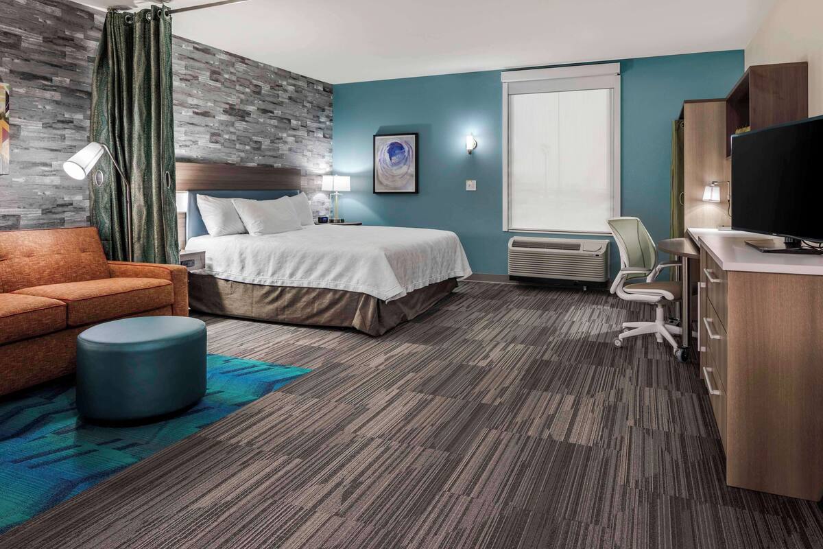 Ein Hotelzimmer mit Bett, Schreibtisch mit Computer, Stuhl, Sofa und Fernseher.