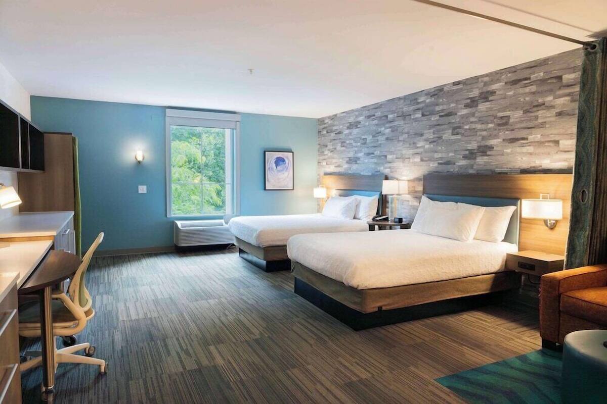 Ein Hotelzimmer mit zwei Betten, einem Schreibtisch, einem Stuhl und einem großen Fenster.