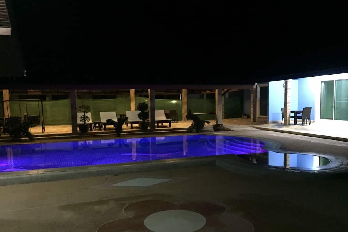 A swimming pool with a blue-lit edge, lounge chairs, and a patio area with tables and chairs.
