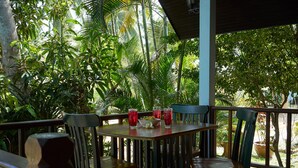 Un espace extérieur aménagé avec des tables et des chaises en bois, entouré d’une végétation tropicale luxuriante.