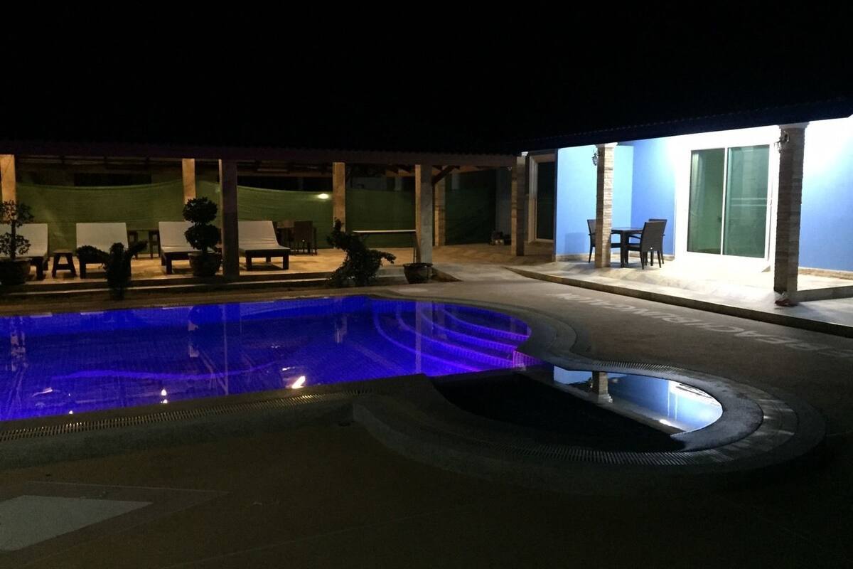 A swimming pool with a blue light feature, surrounded by lounge chairs and a covered seating area.