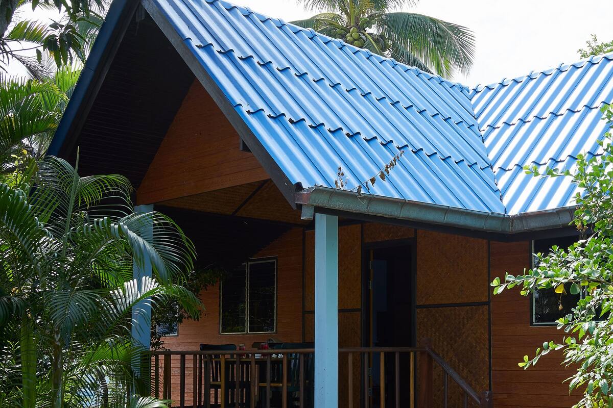 A house with a blue corrugated metal roof, wooden walls, and a porch with a railing.