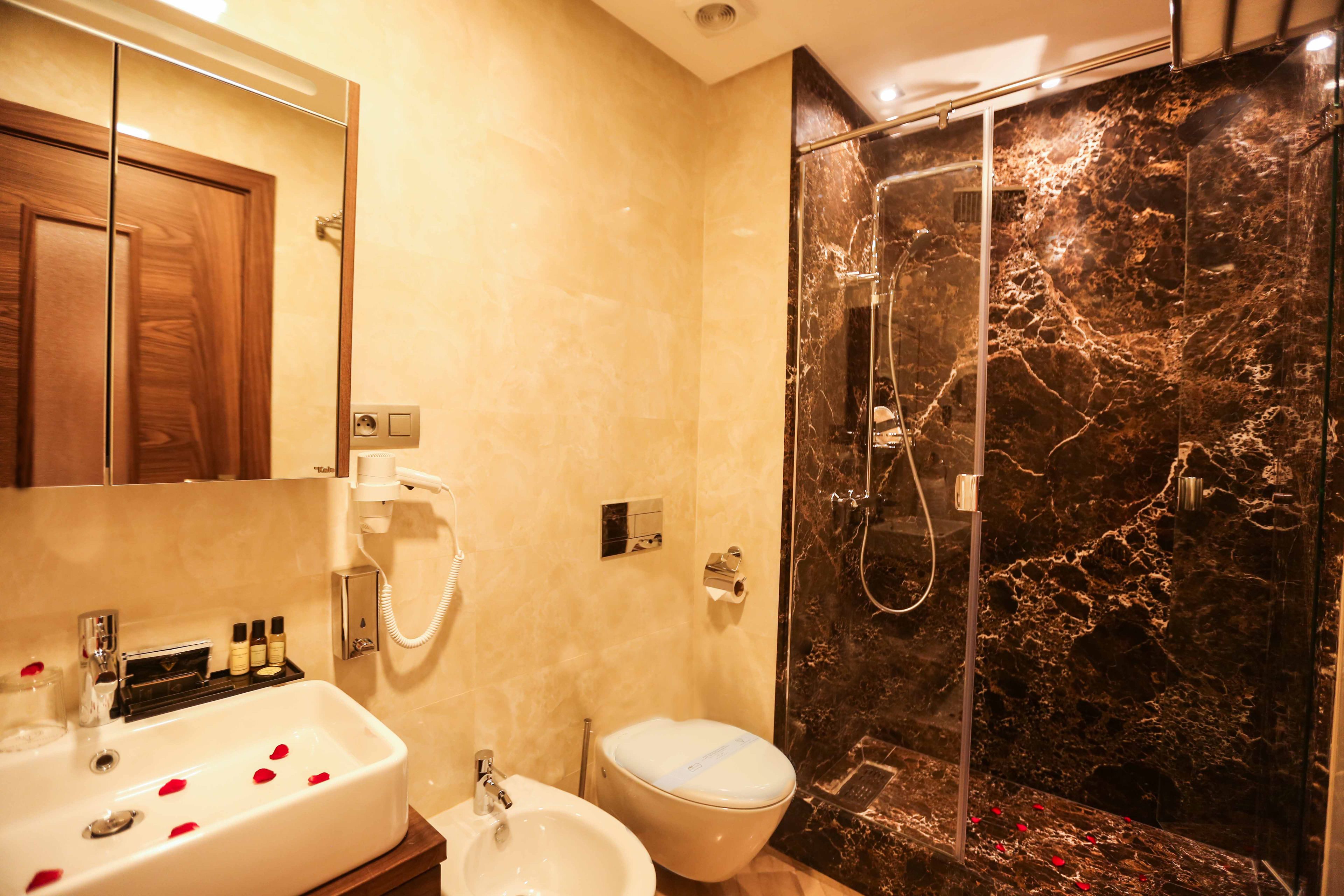 A bathroom with a marble shower, a sink with rose petals, and a toilet.