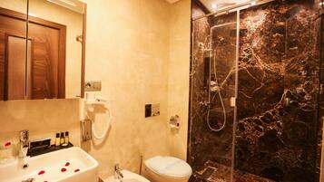 A bathroom with a marble shower, a sink with rose petals, and a toilet.