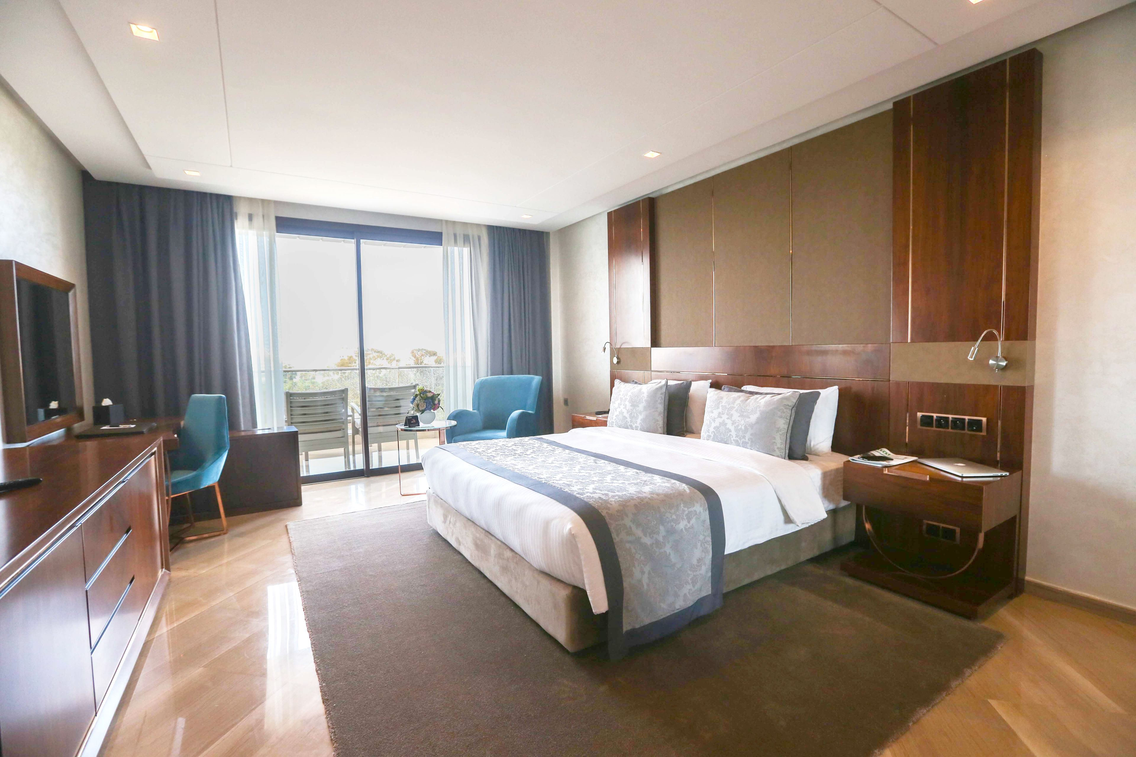 Une chambre d’hôtel moderne, dotée d’un grand lit, d’un bureau, d’une chaise et offrant une vue sur l’extérieur.